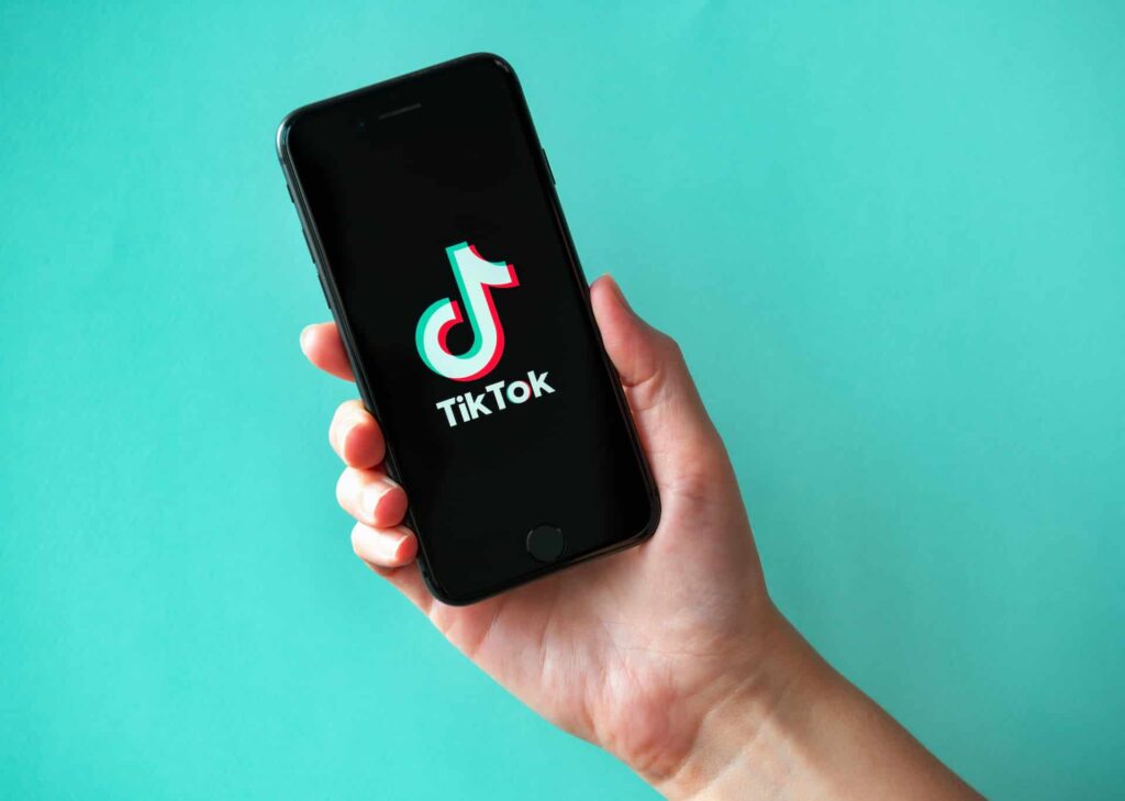 A hand holds a smartphone, showcasing the TikTok logo against a teal background, highlighting the best TikTok tools to enhance your content creation experience.